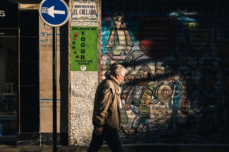 Photo de rue en couleur d'un vieil homme marchant devant une devanture taguée dans les rue de Valence, en Espagne.