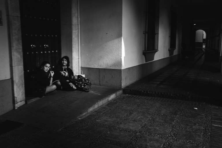 Photo de rue en noir et blanc de deux jeunes filles assises au sol dans une ruelle de Seville en Espagne.