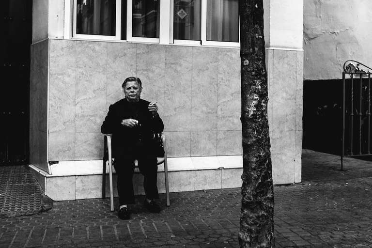 Photo de rue en noir et blanc d'une dame âgée assise sur une chaise en train de fumer une cigarette à Seville en Espagne.