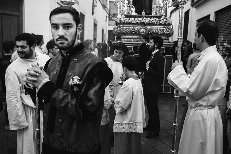 Photo de rue en noir et blanc d'un groupe de jeunes hommes en tenue religieuse pendant une procession dans une ruelle de Cordoue, en Espagne.