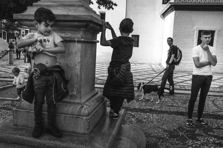 Photo de rue en noir et blanc d'un groupe d'enfant jouant sur un monument devant une église à Grenade en Espagne. 