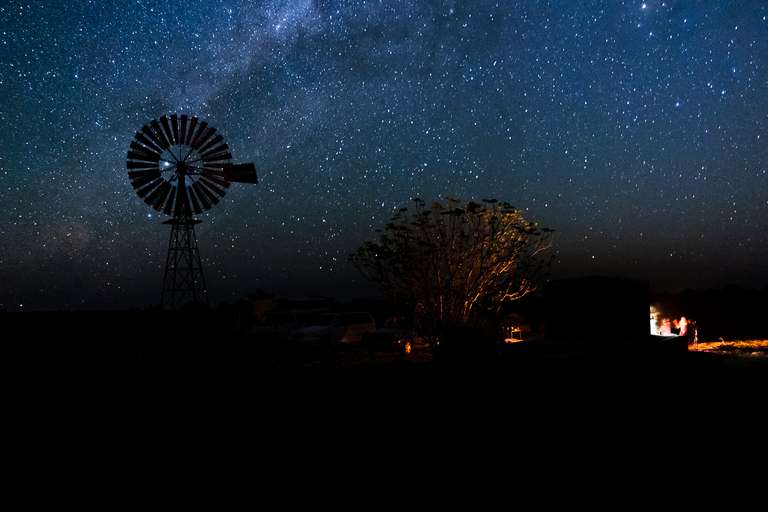 Photo en couleur d'un campement avec un feu de camp sous une éolienne pendant une nuit étoilée avec la voie lactée dans le désert en Asutralie.