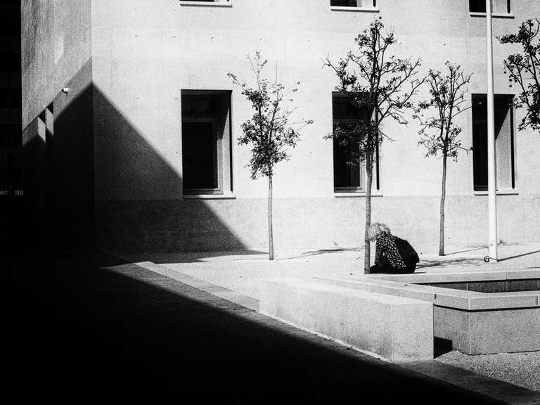 Photo de rue en noir et blanc d'une femme assise sur un banc de béton dans le jardin de la médiathèque de Toulon, dans le sud de la France.