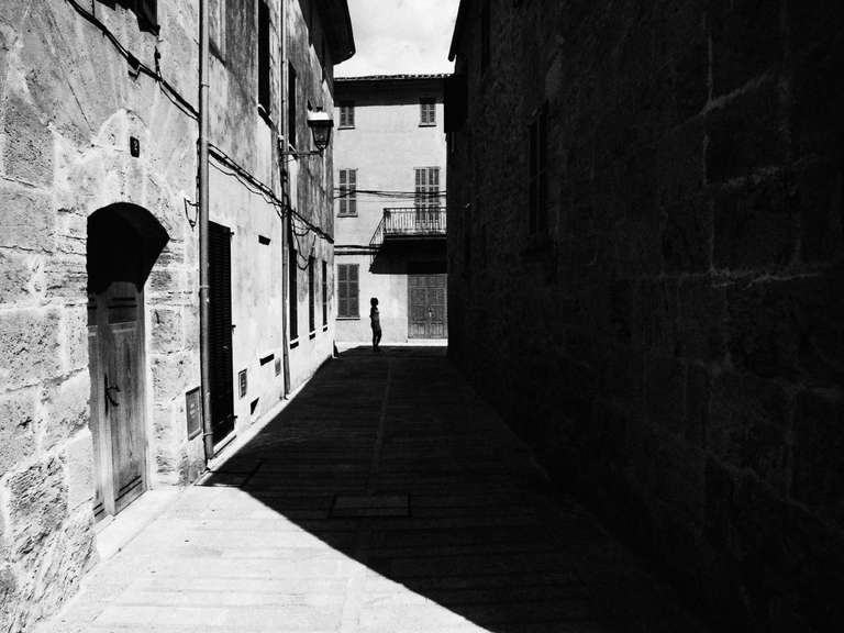 Photo de rue en noir et blanc d'une vielle rue d'Alcudia, avec un enfant en silhouette à Majorque, en Espagne.