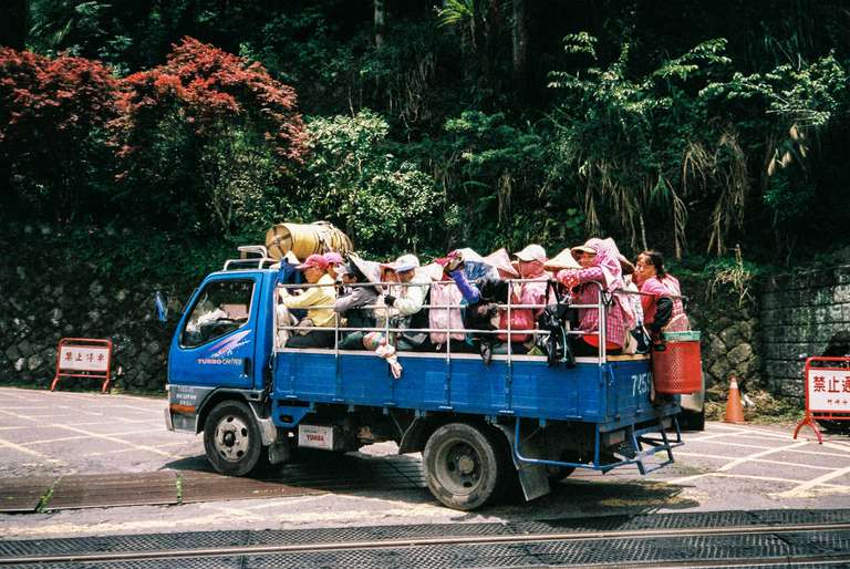 Color photography, a picture of tea worker going up the mountain at the back of a blue truck in Taiwan's mountains.