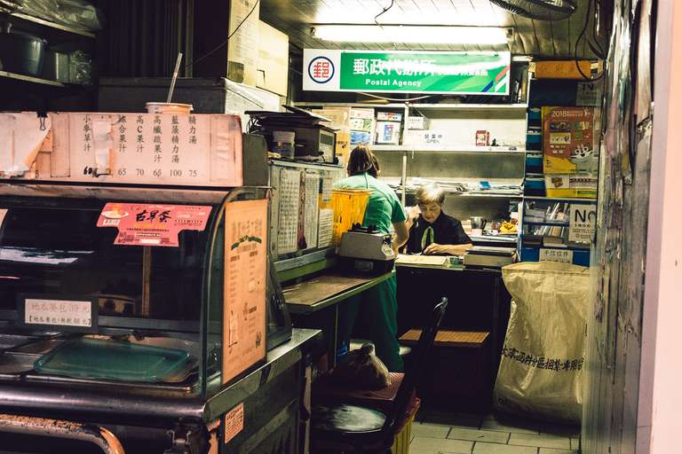 Color street photography. A picture of an old women working inside a tiny post office in the streets of Taipei, Taiwan.