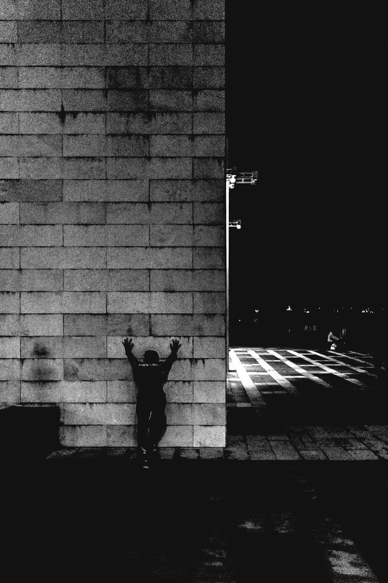Black and white street photography. A picture of a man leaning on a wall at night in Hong Kong.