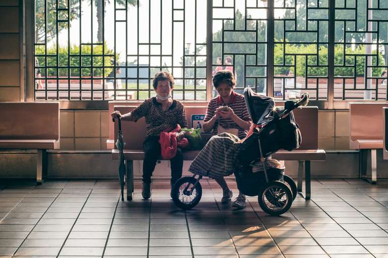 Color street photography. A picture of a couple of old women sitting on a bench at an outdoor metro station with a stroller, in Taipei, Taiwan.