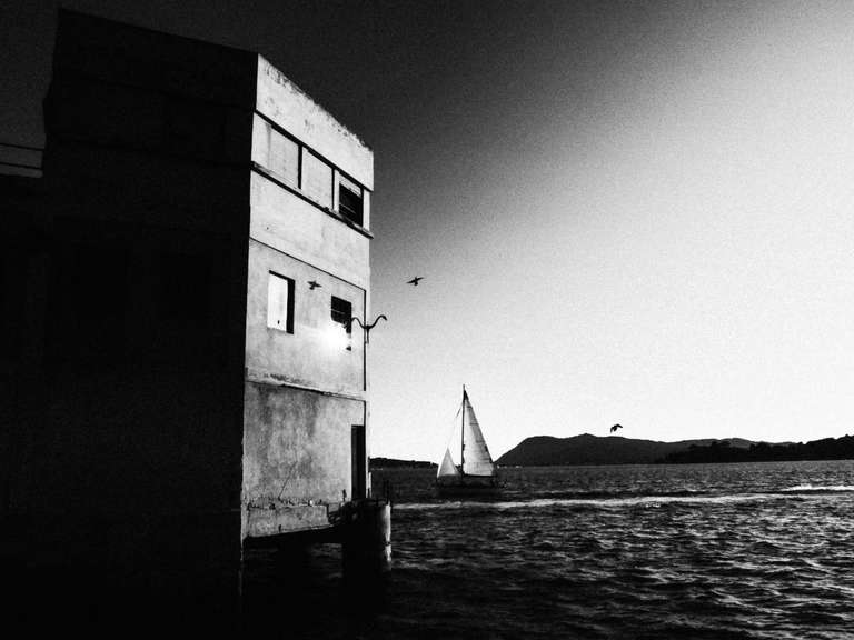 Black and white street photography. A picture of a boat entering Toulon's bay, a bird is flying over. South of France.