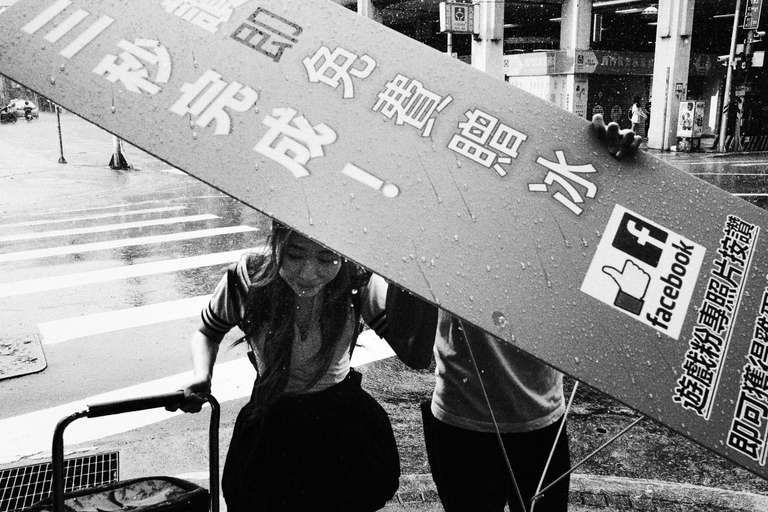 Black and white street photography. A picture of a girl under an ad sign held by a man during a rainy day in Taipei, Taiwan.