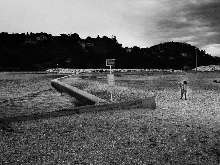 Black and white street photography. A picture of a boy playing near the sea on a cloudy day in Toulon, south of France.