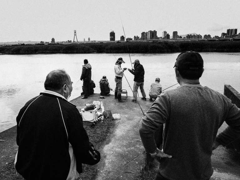 Black and white street photography. A picture of a group of fishermen on the shore of Tamsui river in Taipei, Taiwan.